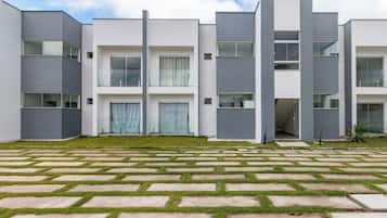 A modern multi-story residential building with a flat roof, large windows, and a paved courtyard with patterned paving.