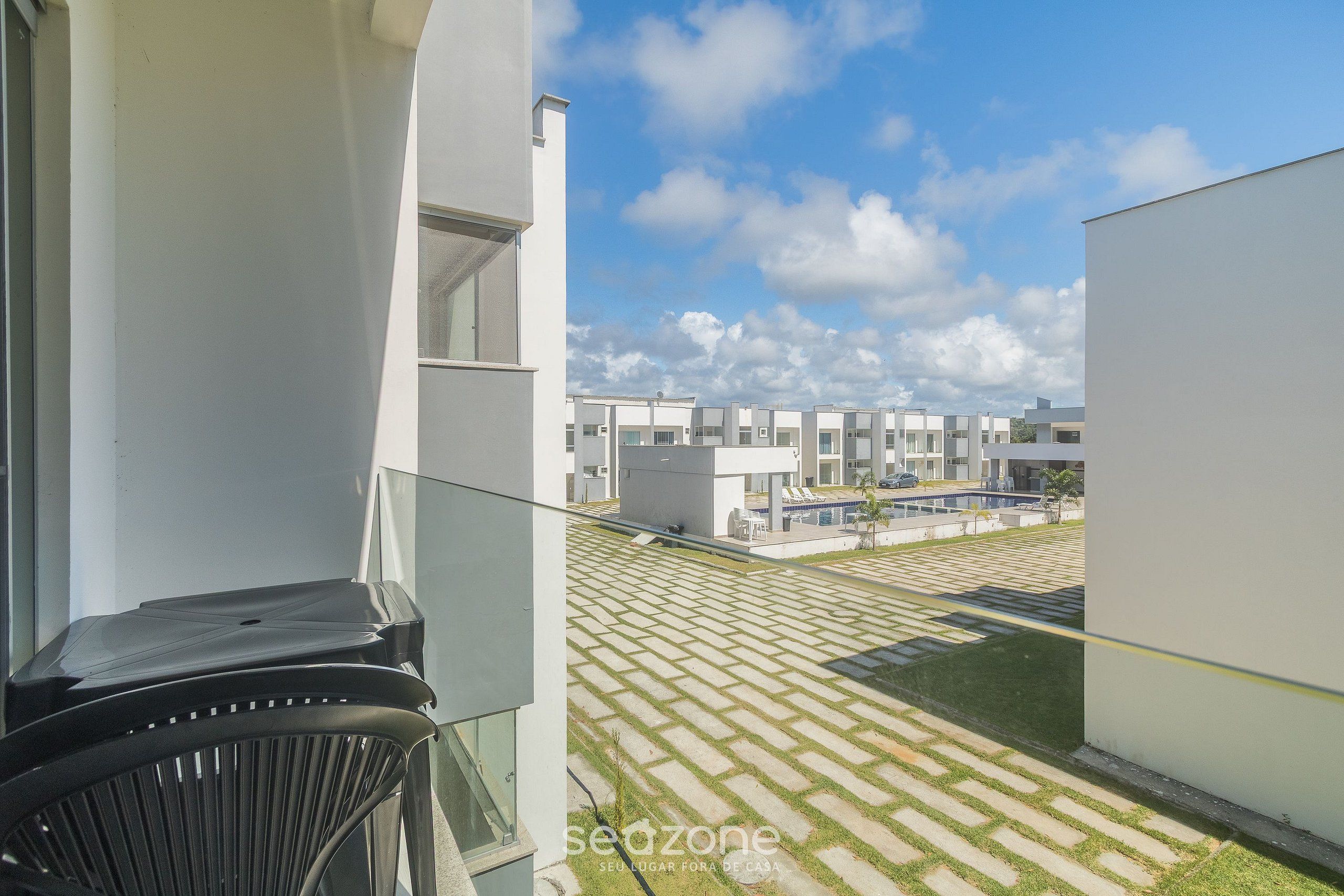 A modern building with a balcony overlooking a courtyard with patterned paving and a pool.