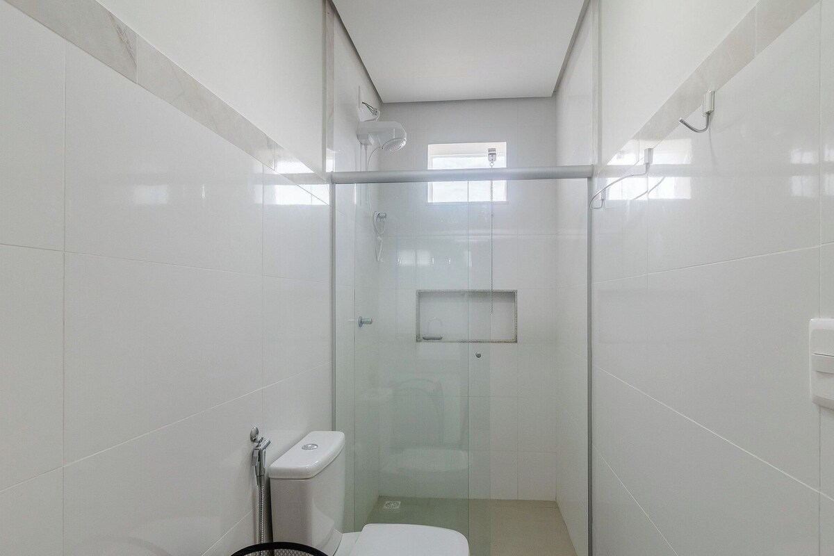 A compact, modern bathroom with a glass-enclosed shower, a toilet, and a small window.