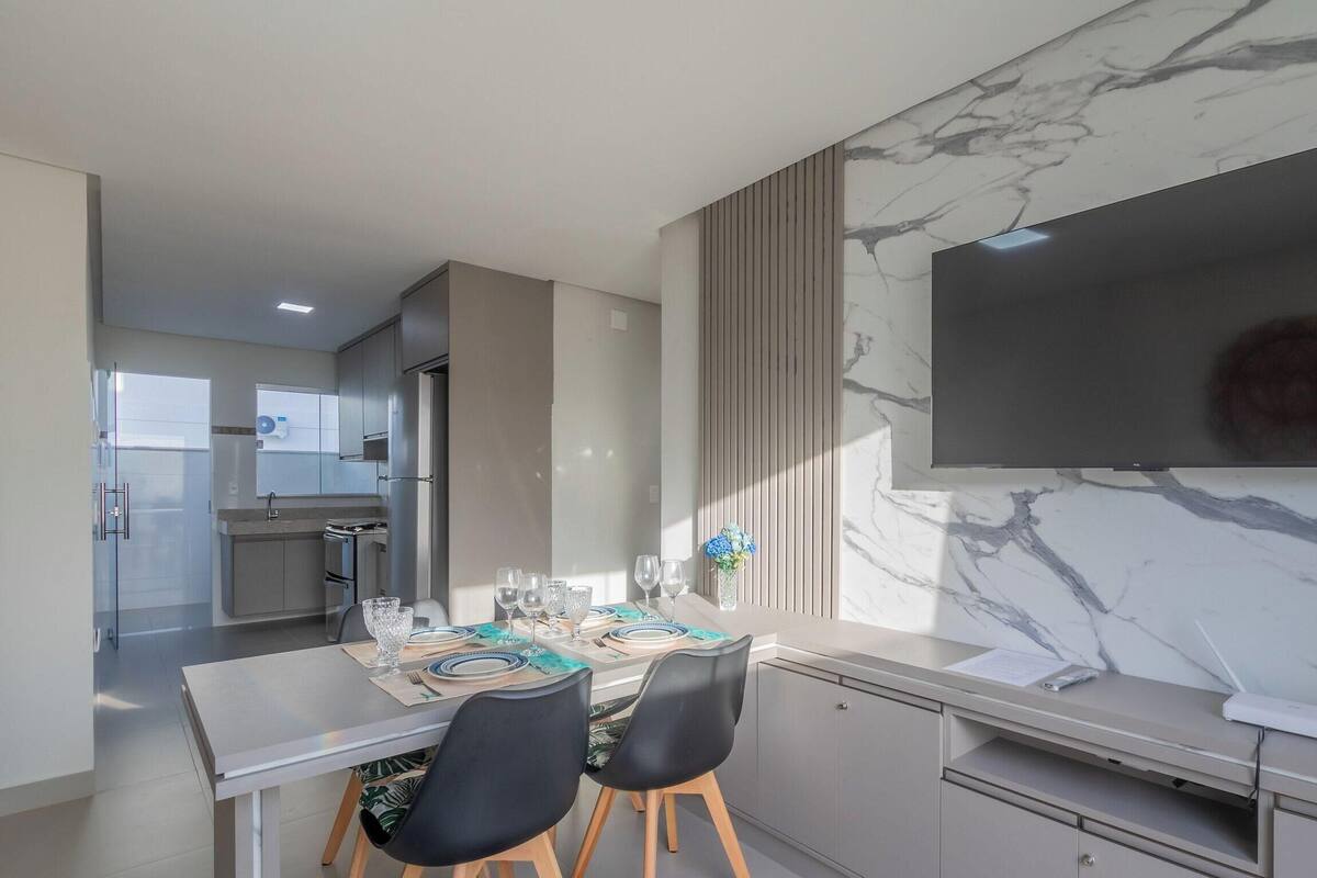 A modern kitchen with a dining area, marble backsplash, and a flat-screen TV.