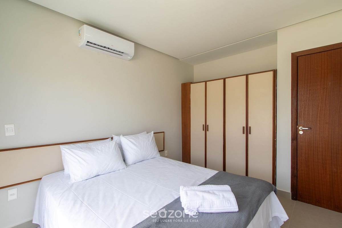 A hotel room with a bed, a wardrobe, and an air conditioning unit.
