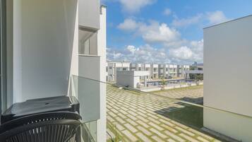 En modern byggnad med en balkong som vetter ut mot en innergård med ett vackert mönstrat gatubelägg och en pool.
