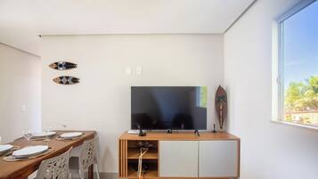 A modern living space with a flat-screen TV mounted on a wooden cabinet, a dining table with chairs, and a decorative wall piece.