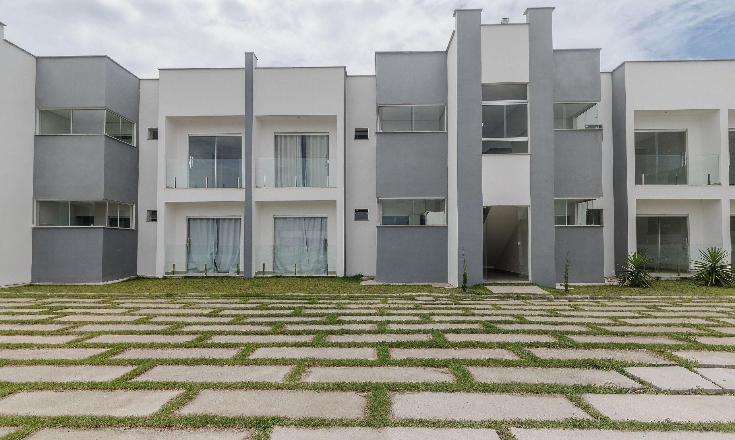 Un immeuble résidentiel moderne à plusieurs étages, doté d’un toit plat, de grandes fenêtres et d’une cour pavée avec une pelouse.