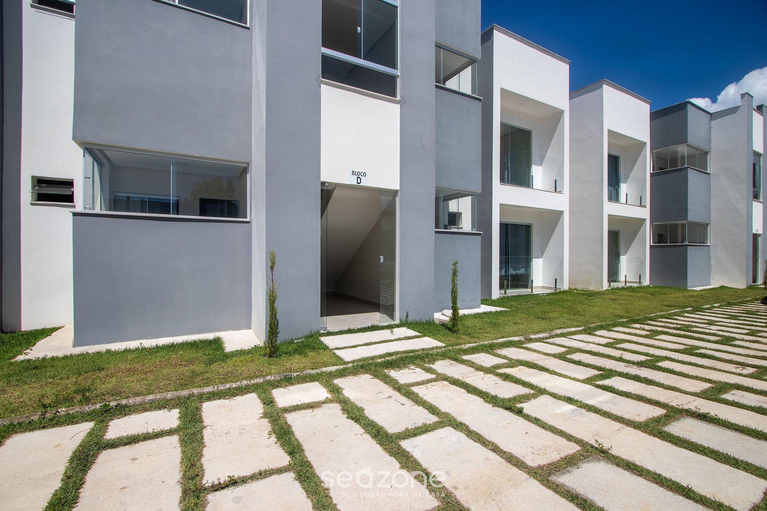 Un edificio moderno con techo plano, ventanas amplias y un patio empavedado con césped y losas de piedra.