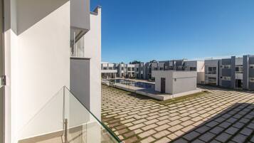 A modern residential building with a paved courtyard and a glass balcony.