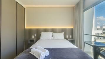 A hotel room with a large bed, a view of the city through a balcony, and a 'sedzone' sign on the bedspread.