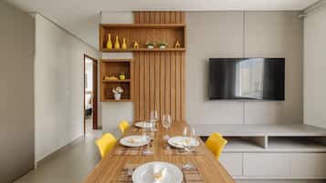 Un'area pranzo moderna con un tavolo in legno apparecchiato per sei persone, una TV a schermo piatto montata a parete e una panca integrata con vano contenitore.