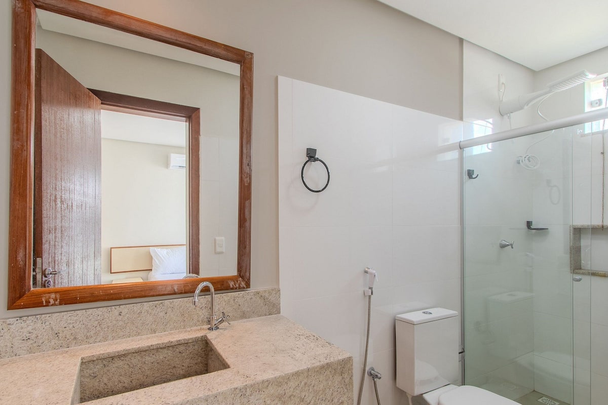 A bathroom with a granite sink, a wooden-framed mirror, a glass shower enclosure, and a toilet.