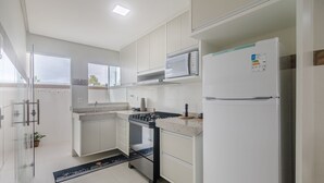 Une cuisine moderne avec des meubles blancs, un four à micro-ondes encastré, une cuisinière à gaz et un réfrigérateur.