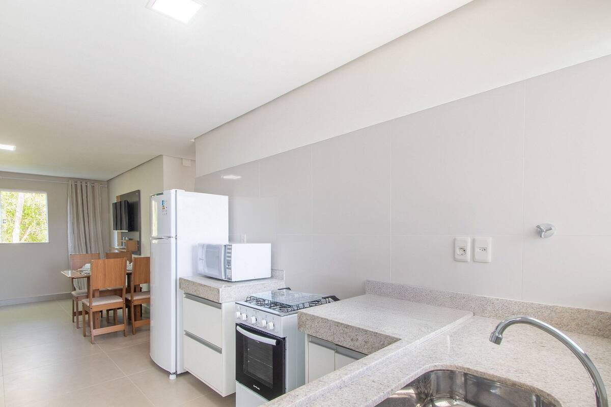 A modern kitchen with a gas stove, oven, refrigerator, and microwave. There is a dining area with chairs and a table, and a window providing natural light.