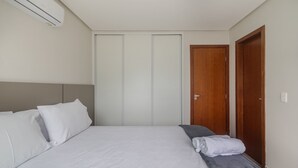 Une chambre à coucher avec un lit, des oreillers, une table de chevet, une serviette, une porte en bois et un appareil de climatisation.