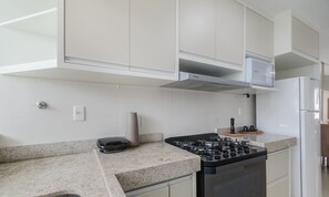 A kitchen with white cabinets, a gas stove, a built-in oven, and a microwave. - Apartments Near Muta Beach, BA - Rfms (Porto Seguro)