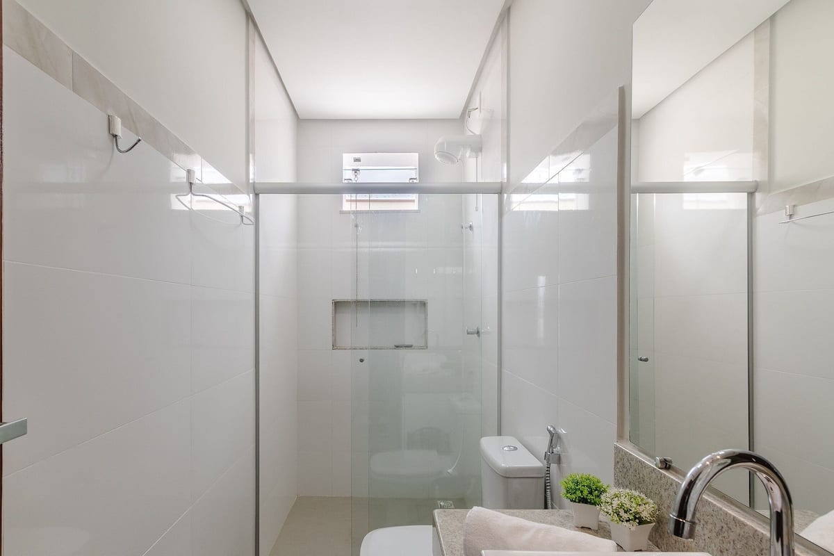A modern bathroom with a glass-enclosed shower, a toilet, a sink with a mirror, and a small window for natural light.