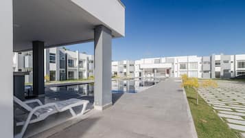 A modern building with a pool area, outdoor seating, and a clear sky.