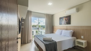Una camera d'albergo con un letto, un comodino, un condizionatore d'aria a parete, un quadro e vista sul verde.