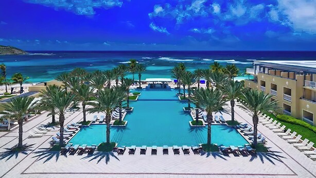 Zwembad van een resort met uitzicht op de oceaan en palmbomen.