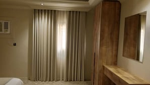 Een hotelkamer met een bed, een houten bankje, een grote spiegel en een raam met gordijnen.