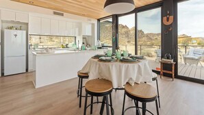 A modern kitchen with white cabinets, a central island, and a dining area with stools. - Late for the Sky • Modern Marvel with Hot Tub (Joshua Tree)