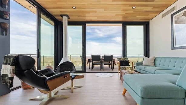 A modern living room with a large window, a sofa, a chair, and a dining area. - Late for the Sky • Modern Marvel with Hot Tub (Joshua Tree)