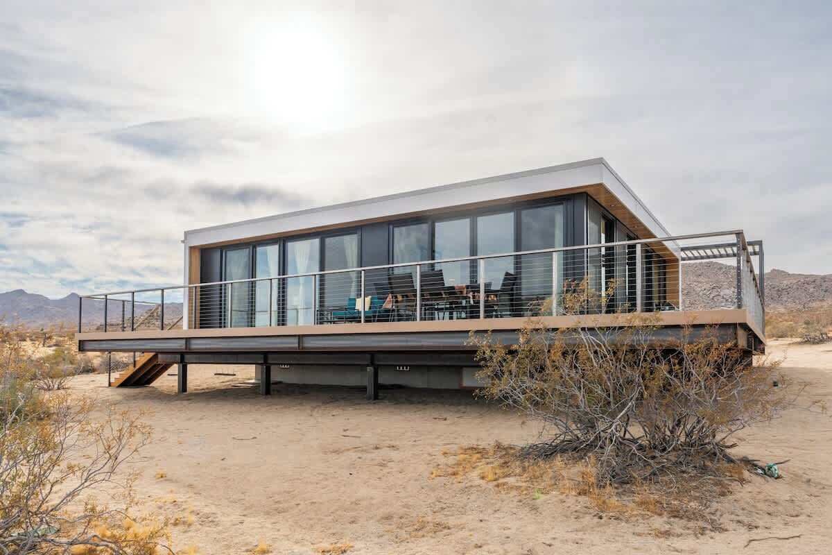 A modern building with large glass windows, a wooden deck, and a desert landscape in the background.