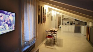 A dining area with a table and chairs, a television mounted on the wall, and a kitchen in the background. - Willy's Home (Salerno)