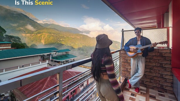 A balcony with a scenic view of mountains and a person playing a guitar. - goSTOPS Mcleodganj, Mall Road (McLeod Ganj)