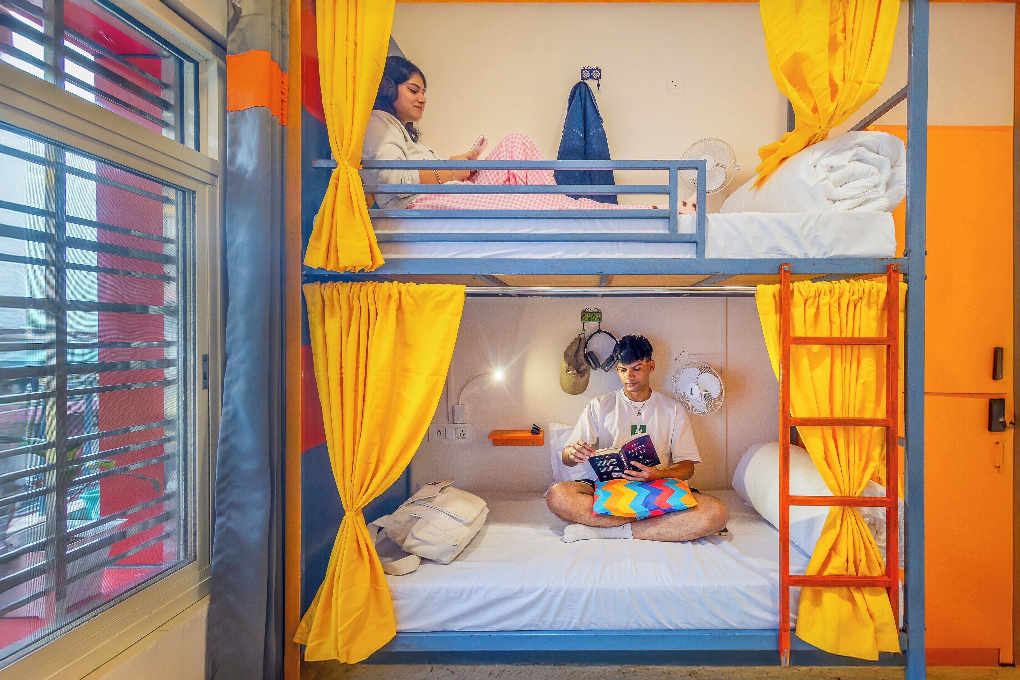 A bunk bed room with yellow curtains, a fan, and a window with blinds.
