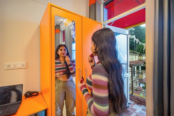 A room with a laptop on a desk, a mirror, and a view of a balcony with a railing. - goSTOPS Mcleodganj, Mall Road (McLeod Ganj)