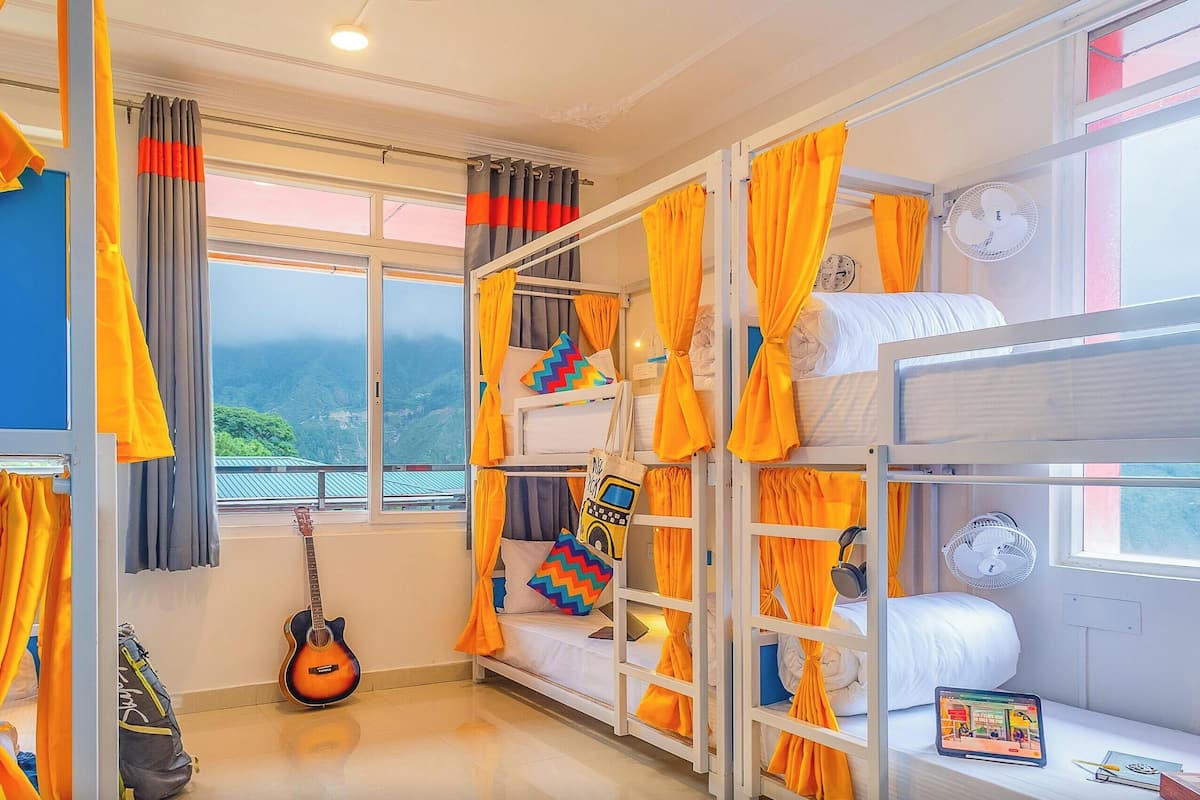 A dormitory room with bunk beds, privacy curtains, and a guitar.