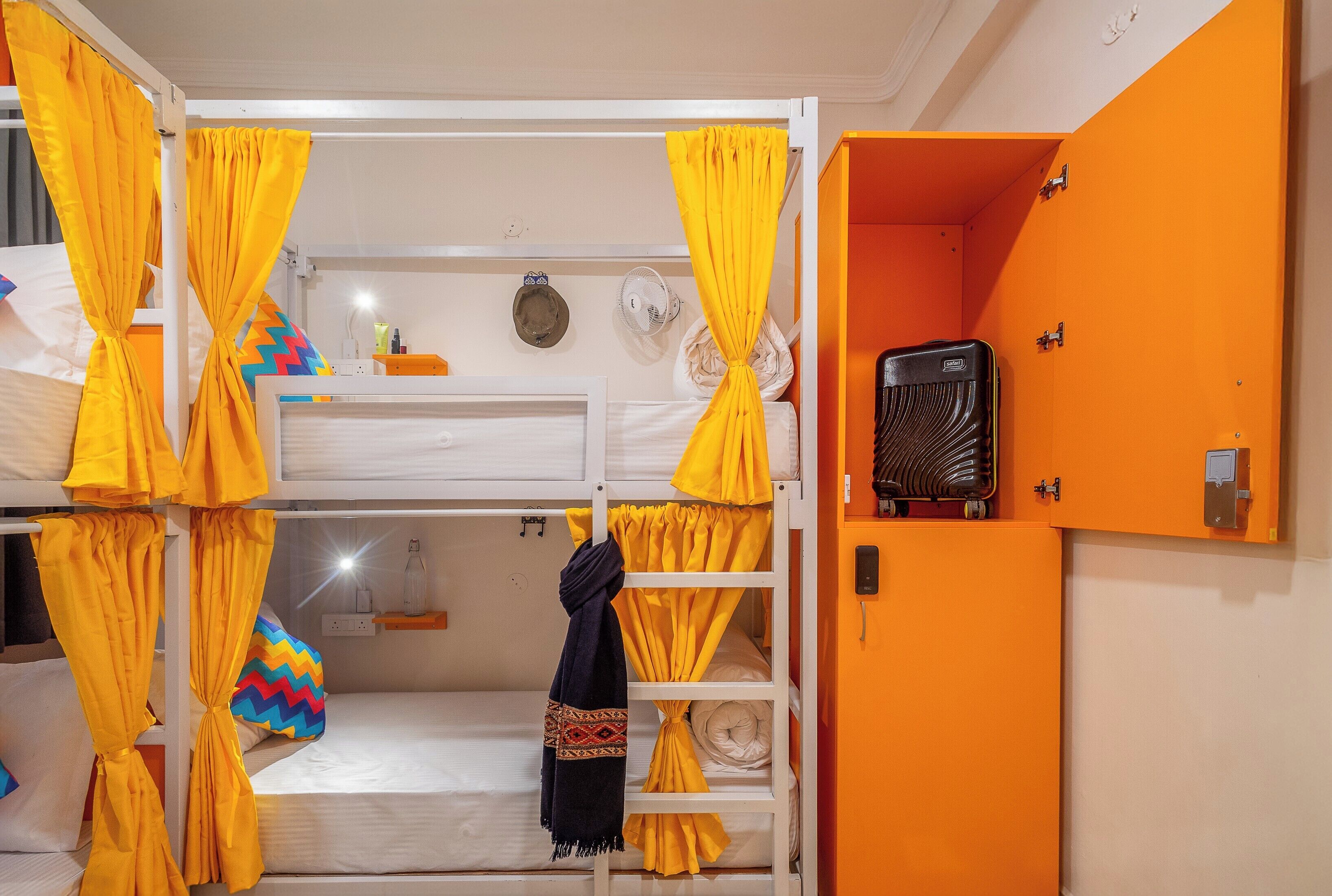 Habitación con literas, cortinas amarillas, una radio y un estante pequeño con artículos de tocador.