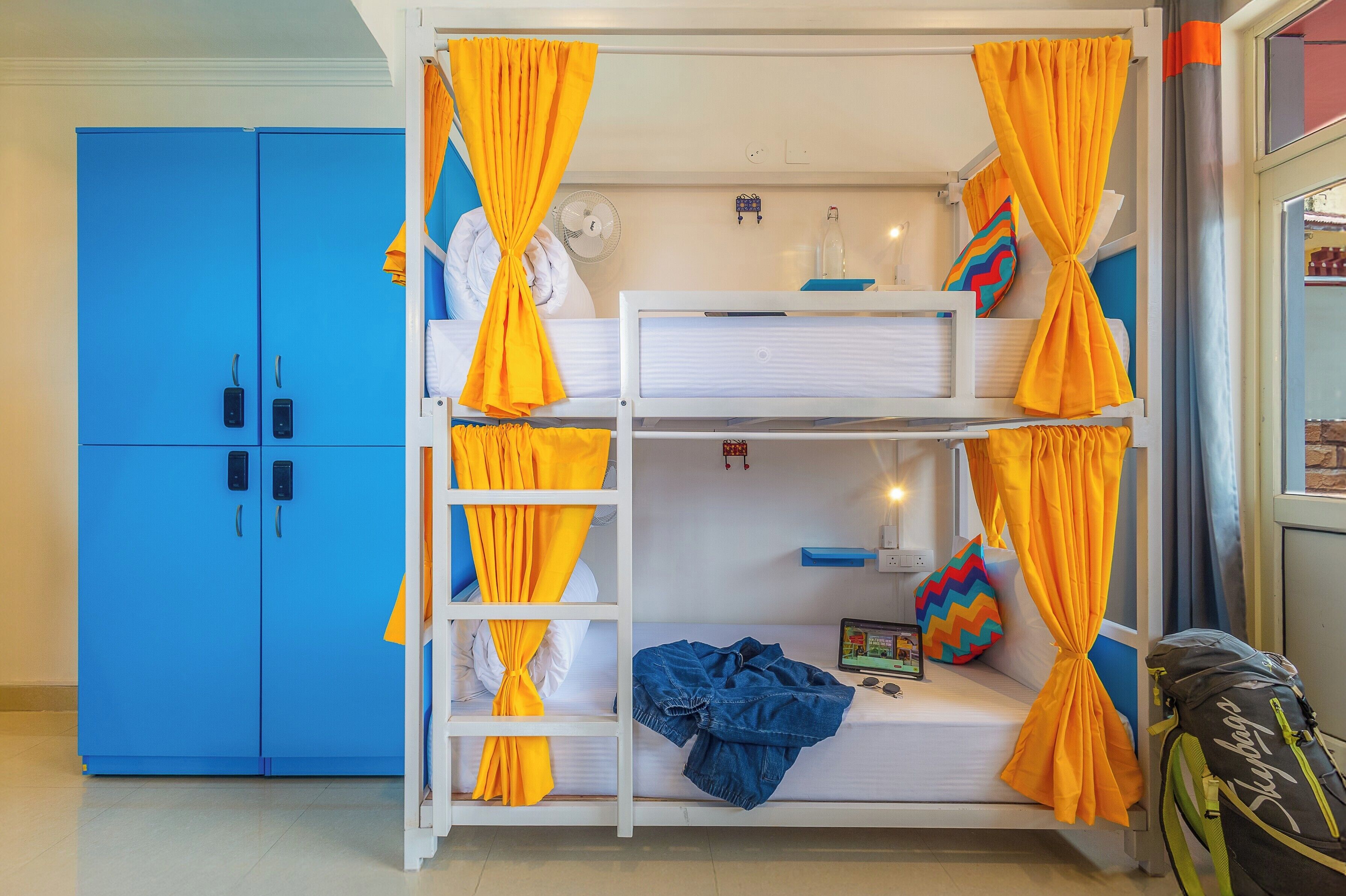 A bunk bed with yellow curtains, a blue wardrobe, and a backpack on the floor.