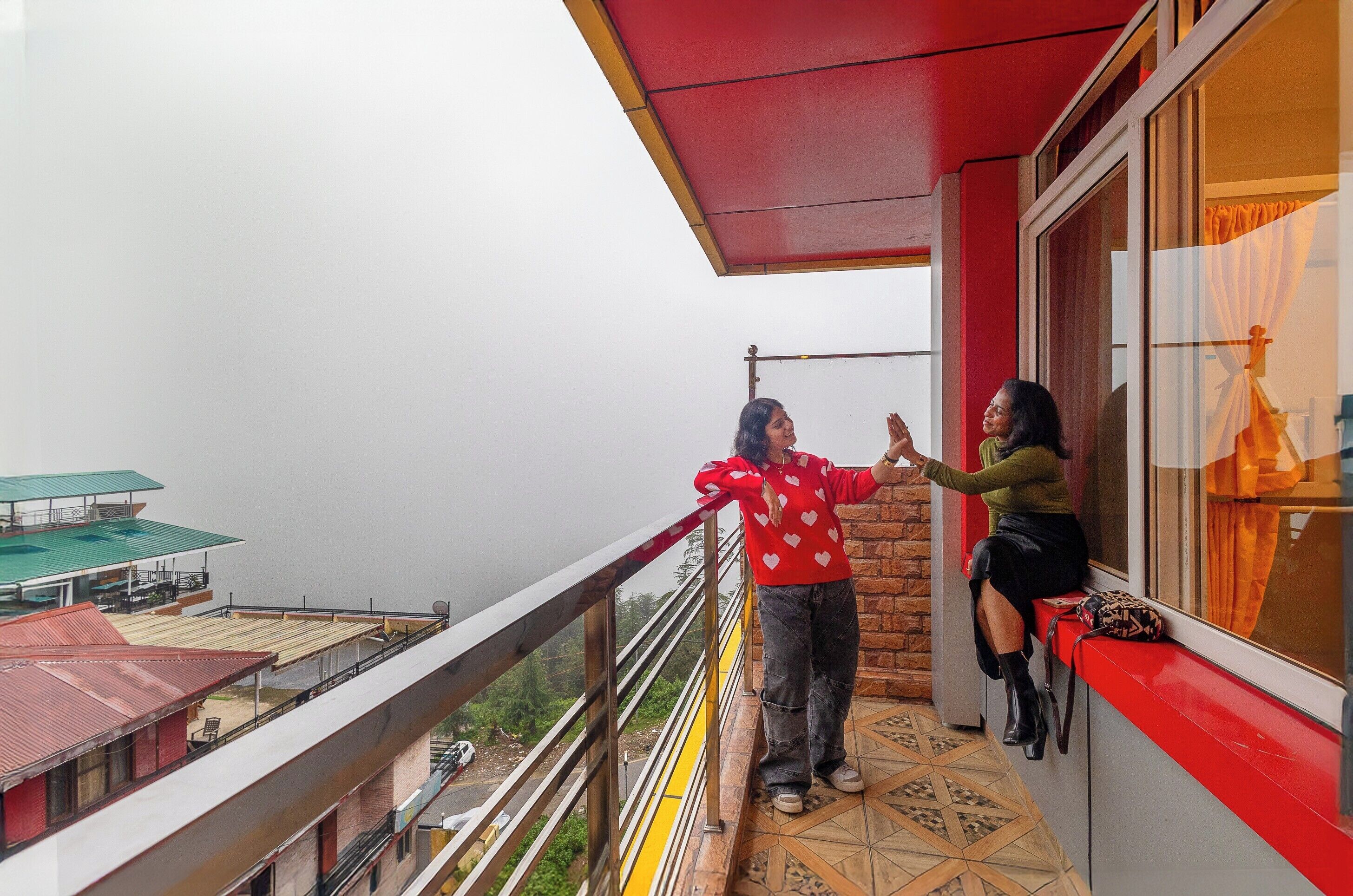A balcony with a red railing, a person standing, and another sitting by a window.