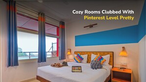 A neatly made bed with pillows and a bedside table, a window with curtains, and a blue accent wall. - goSTOPS Mcleodganj, Mall Road (McLeod Ganj)