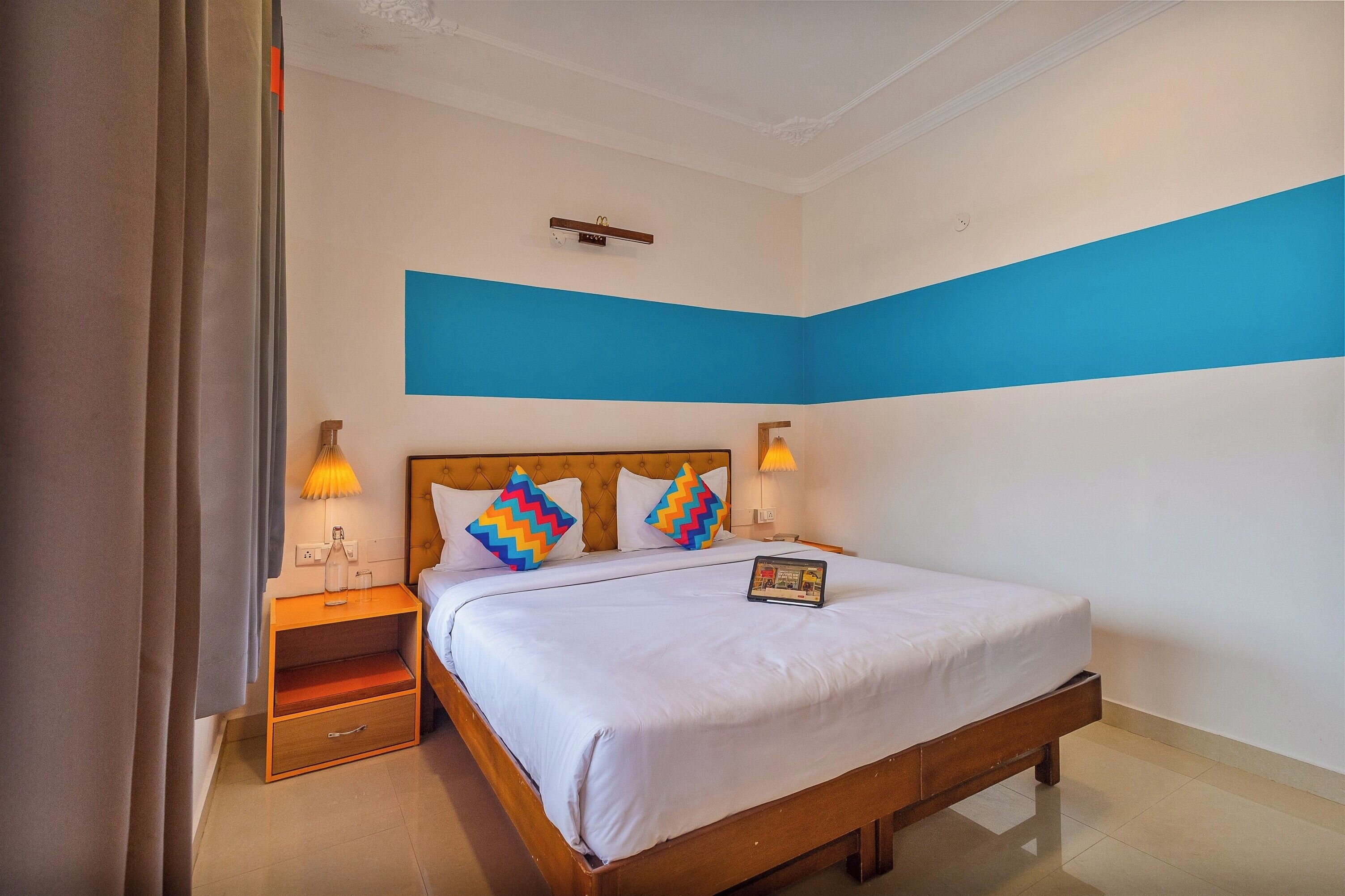 A hotel room with a bed, nightstands, and a wall with a blue stripe.