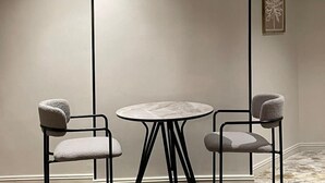 A minimalist room with a round table and two chairs, a single light source, and a wall-mounted artwork. - Haza Manzeli Rabwa Branch (Madinah)