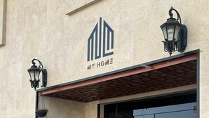 A building entrance with a modern design, featuring a large potted plant and two wall-mounted lanterns. - Haza Manzeli Rabwa Branch (Madinah)