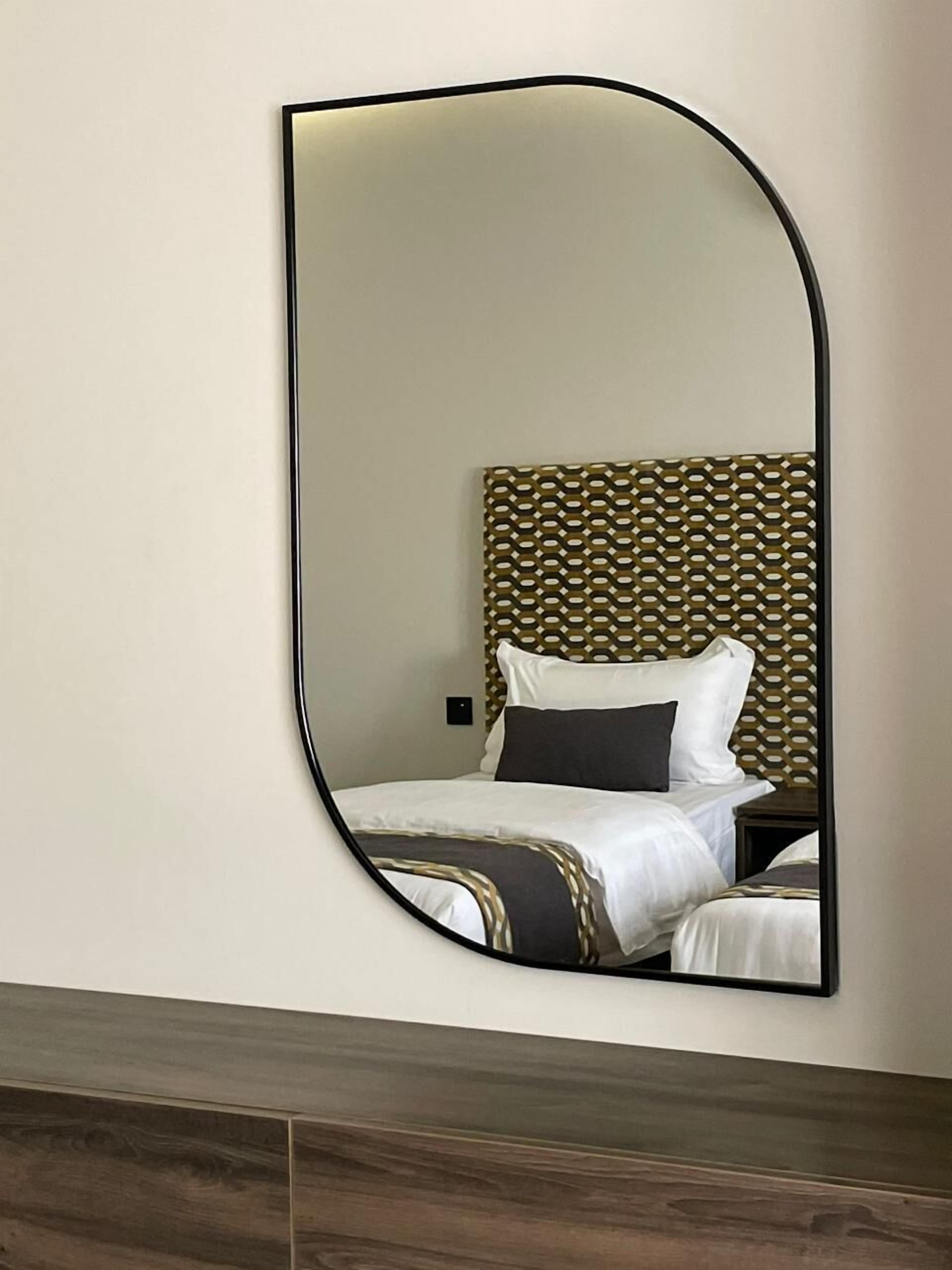 Een kamer met een grote spiegel, een bed met wit beddengoed, een gestreept hoofdeinde en een houten vloer.