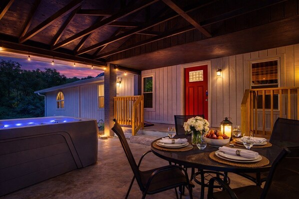 An outdoor dining area with a table set for two, a hot tub, and a red door.