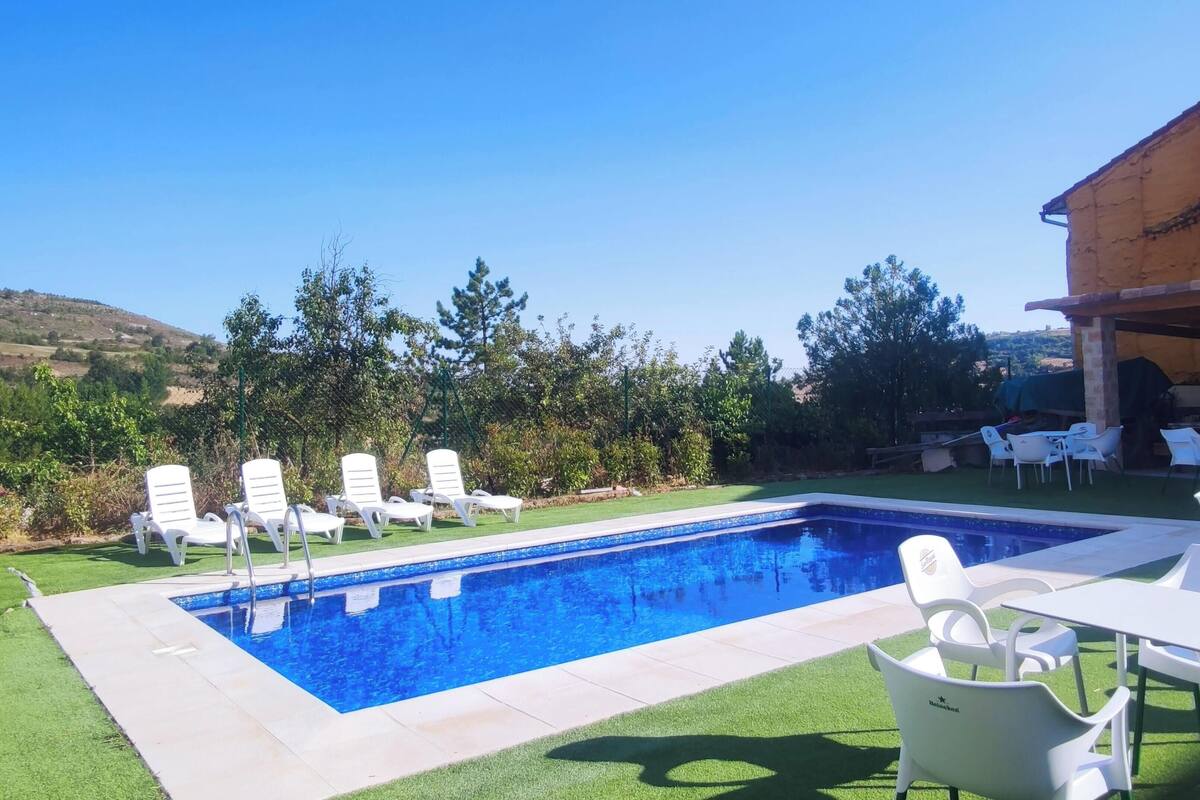 Piscina retangular com superfície de água azul translúcida, rodeada por espreguiçadeiras brancas e uma pequena mesa.