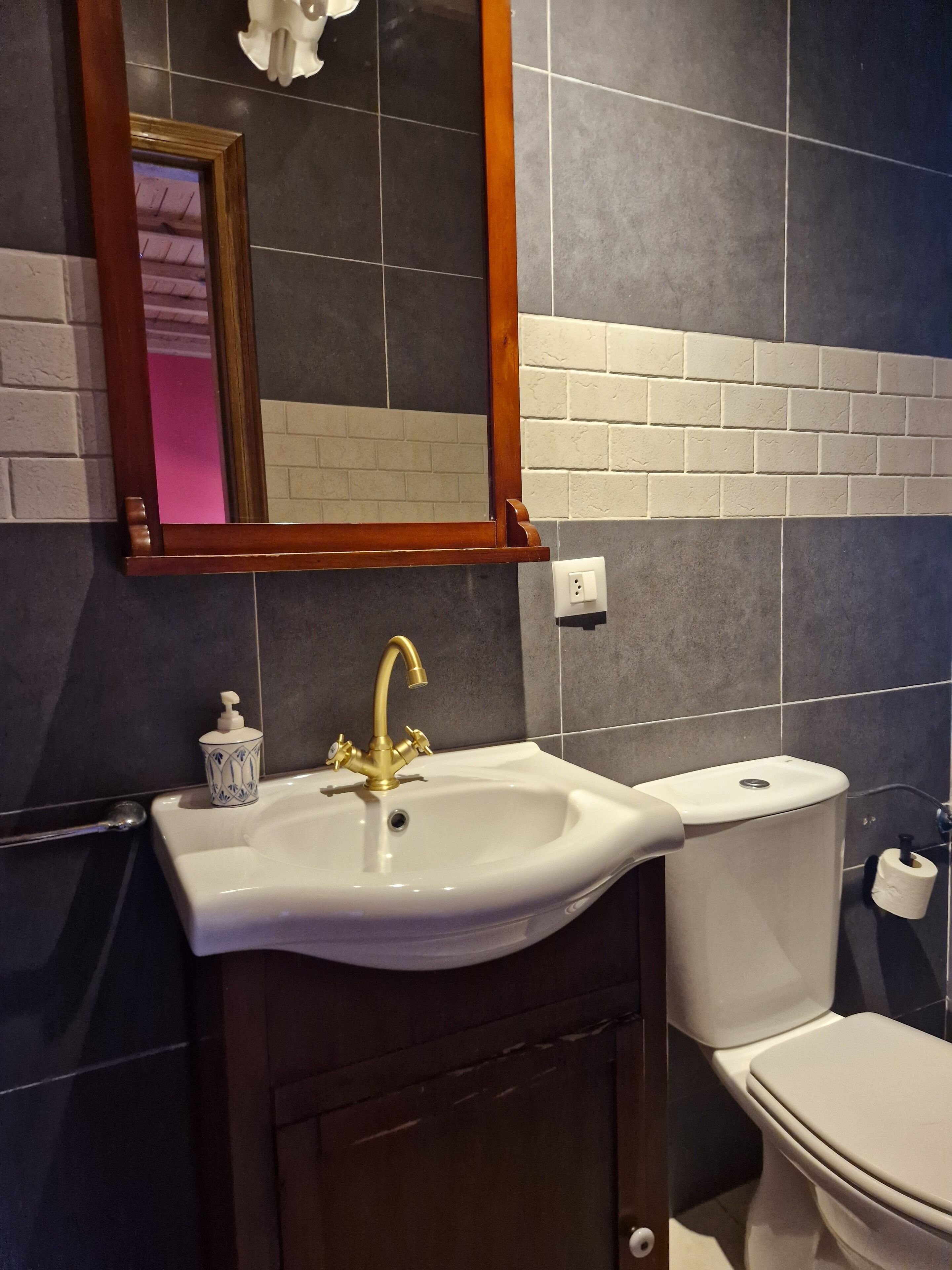 A bathroom with a white sink, gold faucet, and a mirror above it.