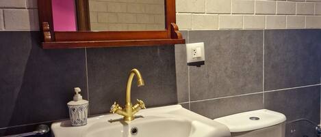 A bathroom with a white sink, gold faucet, and a mirror above it.