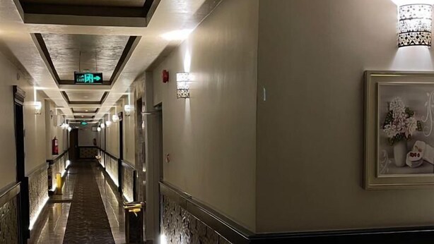 Un couloir d’hôtel avec un tapis à motifs, des appliques murales et un panneau décoratif orné de motifs floraux.