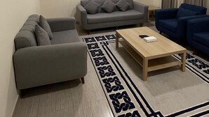 Un salon avec un canapé gris, un canapé bleu, une table basse en bois et un tapis à motifs.