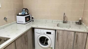 Una cocina compacta con lavadora integrada, un microondas y un lavabo.