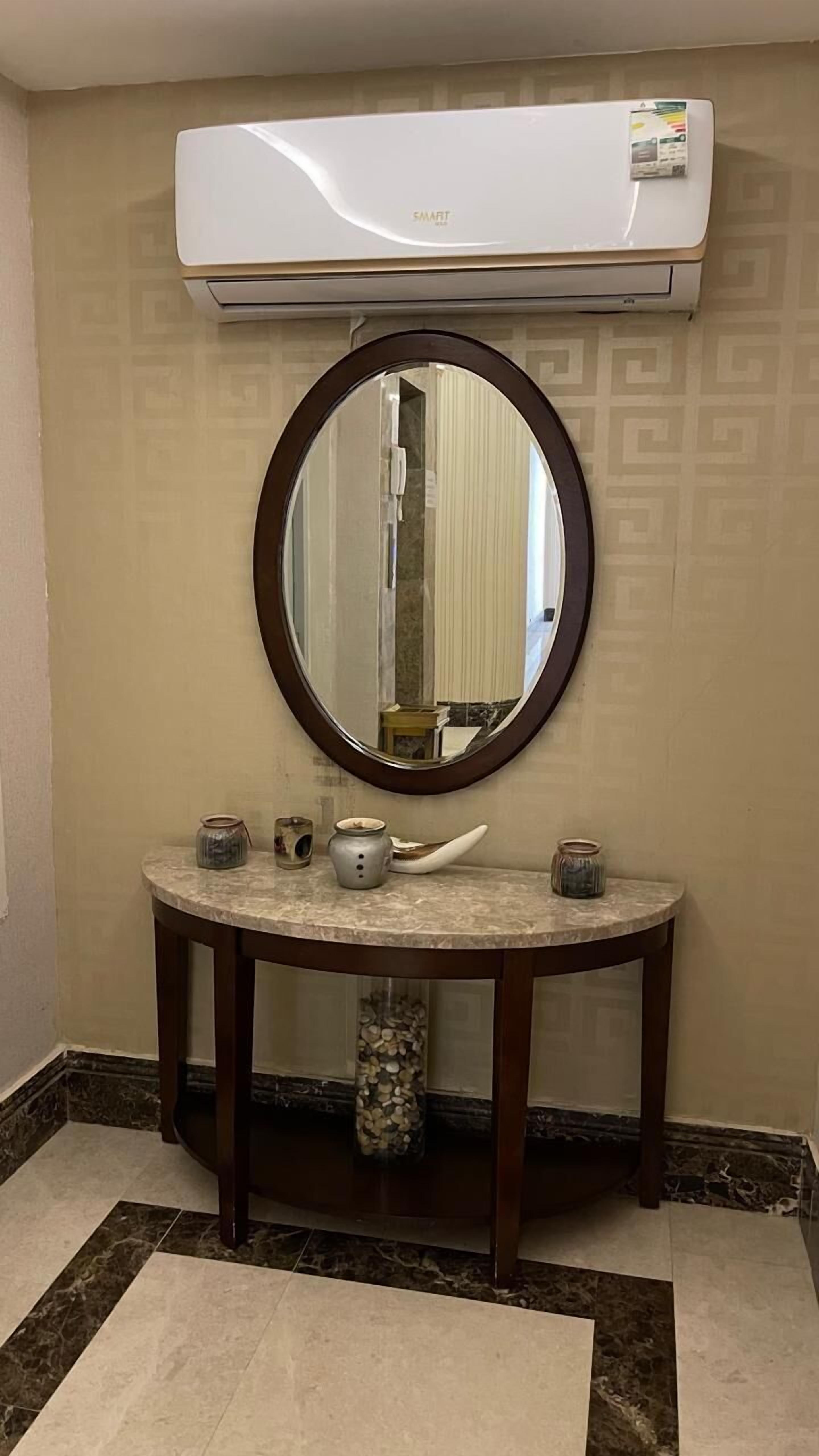 Un baño con un espejo redondo, un lavabo de mármol y una jarrón empotrado.