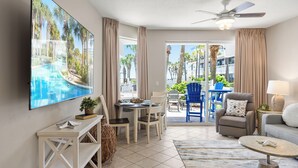 A modern living room with a flat-screen TV, a dining area with chairs, a sofa, and a ceiling fan. - Destin West G116~ Ground Floor ~ Beachfront ~ Handicap Accessible! (Fort Walton Beach)