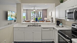 A modern kitchen with white cabinetry, a black stove, and a large window with a view of palm trees and a pool. - Destin West G116~ Ground Floor ~ Beachfront ~ Handicap Accessible! (Fort Walton Beach)