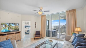 A spacious living room with a television, a ceiling fan, a glass coffee table, and a sofa.