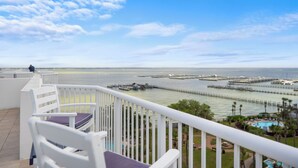 A balcony with white railings, a white chair with a purple cushion, and a view of a marina with boats and docks.